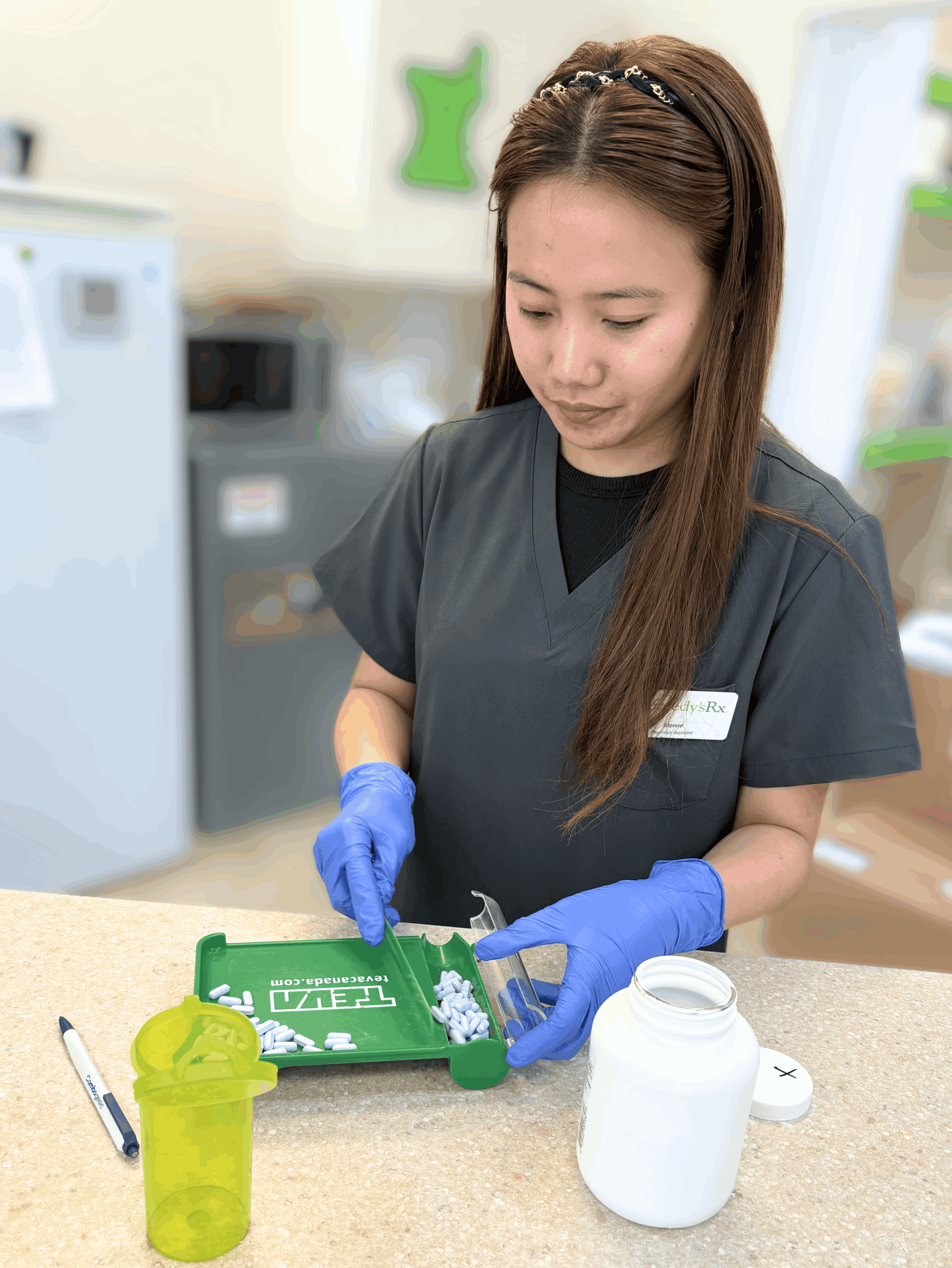 Pharmacy assistant counting pills using a tray and spatula while wearing gloves