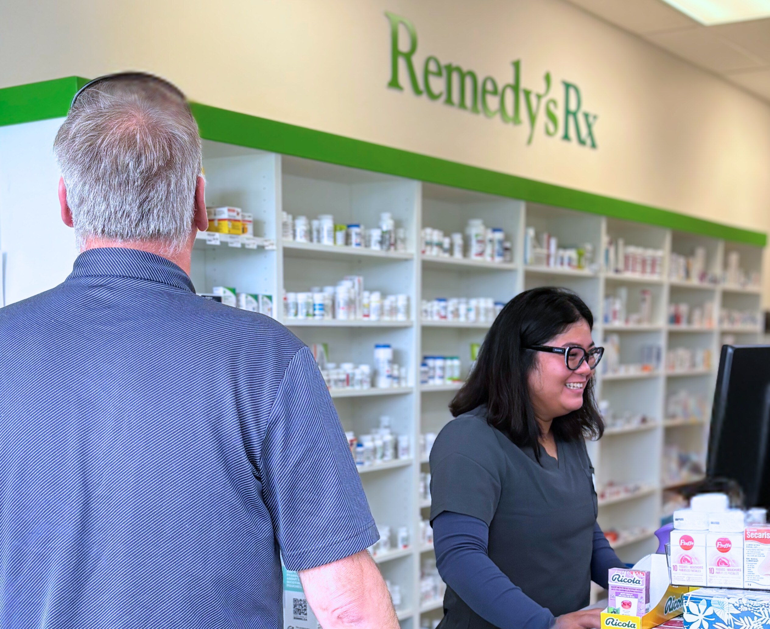 Pharmacy assistant smiling while helping a customer at the counter.